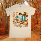 T-shirt with autumn-themed design featuring boots, a hat, and pumpkins against a forest background.