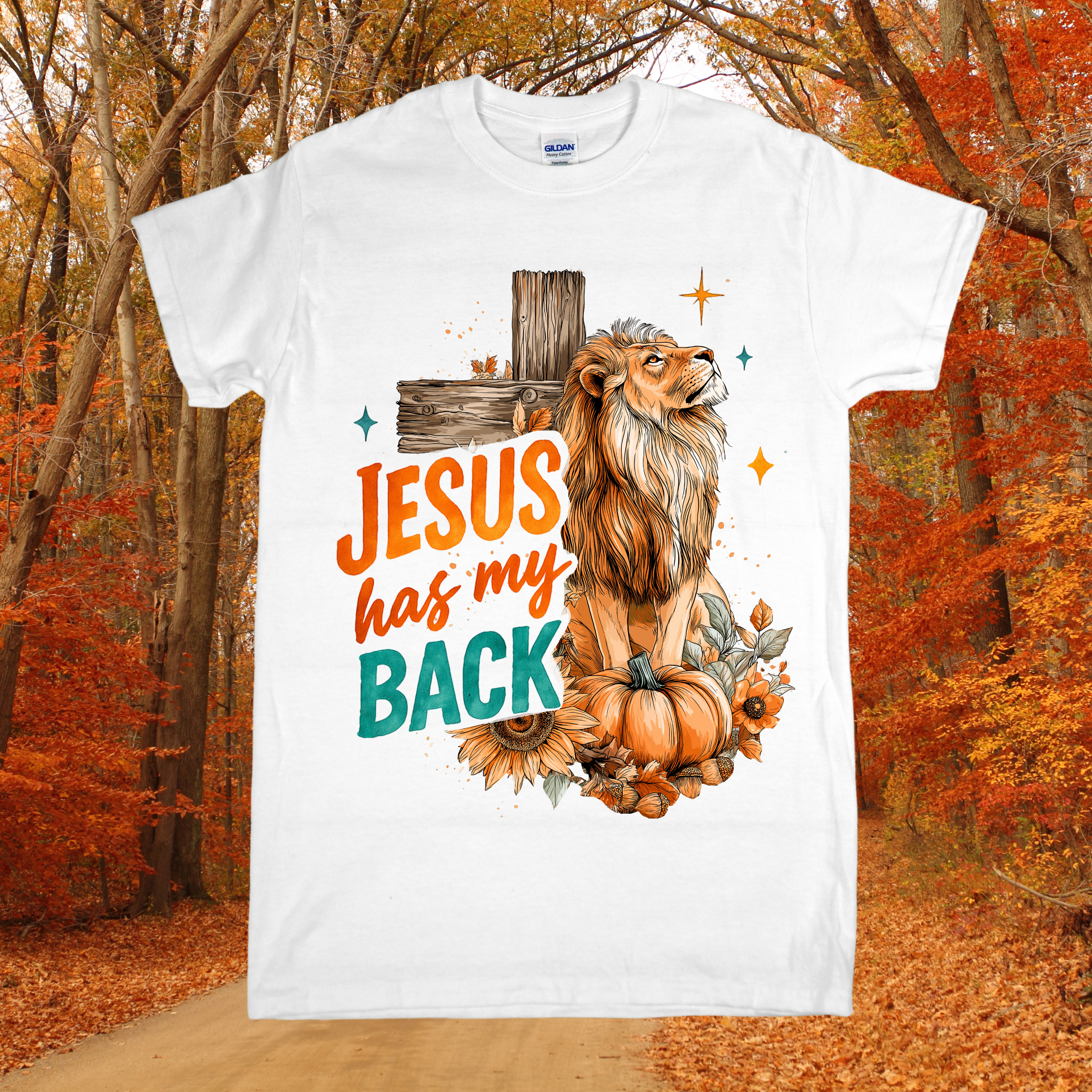 White t-shirt with a lion, pumpkin, and 'Jesus has my back' text in an autumn forest setting.